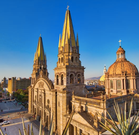 The Guadalajara Cathedral with its neo-Gothic towers, yellow-tiled spires, and large dome, set against a clear blue sky.