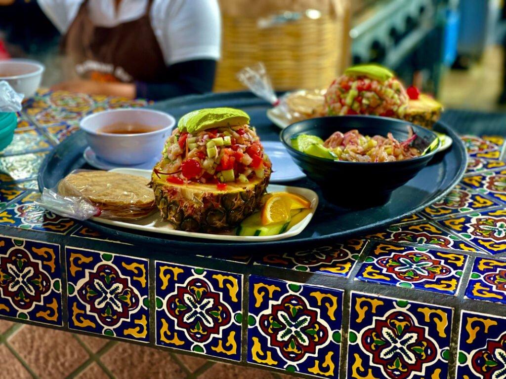 A decorative tiled table showcasing a vibrant and inviting meal presentation with hollowed-out pineapples filled with a colorful mix of diced vegetables and possibly seafood, topped with avocado slices, reflects the fresh ingredients and traditional serving styles of Mexico wine tours.