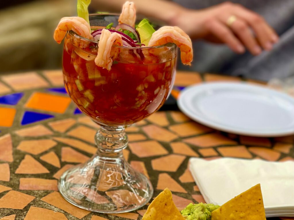 A glass goblet filled with shrimp cocktail, complete with tortilla chips and guacamole, captures the vibrant culinary culture of Mexico wine tours.