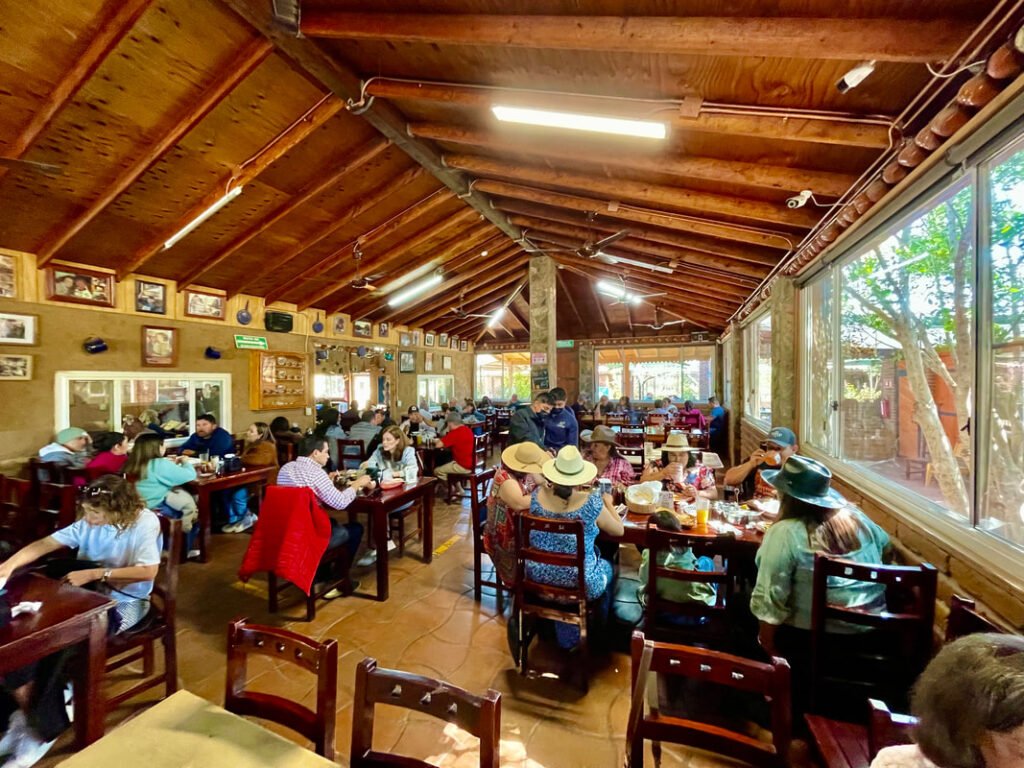 A bustling dining area with wooden interiors, filled with people enjoying their meals and conversations, embodies the lively and social atmosphere of Mexico wine tours.