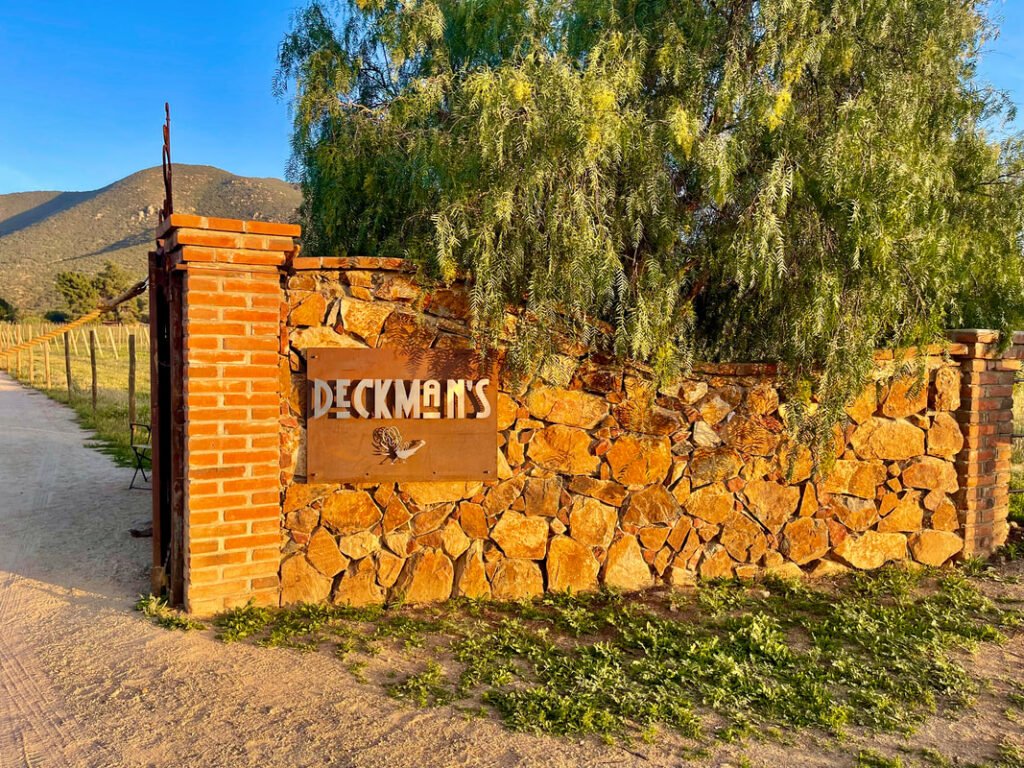 The welcoming stone entrance with a sign reading "DECKMAN'S" and lush greenery overhead embodies the inviting ambiance of Mexico wine tours.