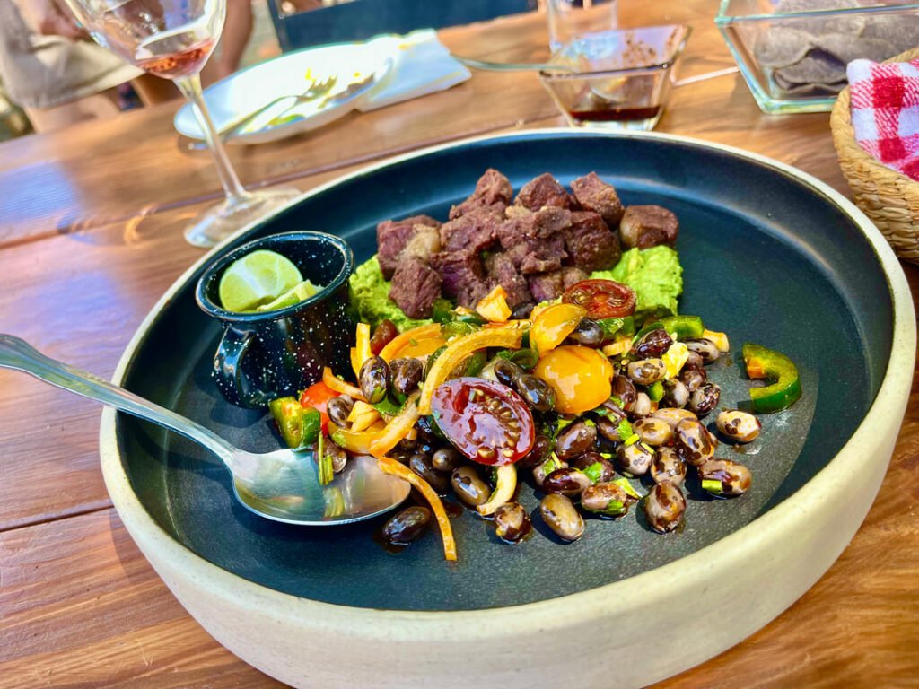 Plate of bean salad, diced meat, guacamole, and a lime wedge in a small cup.