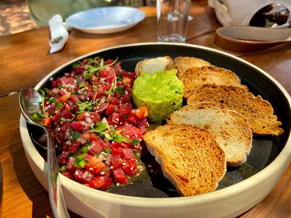 Plate of tuna tartare with microgreens, avocado in the center, and crostini slices on the edge.