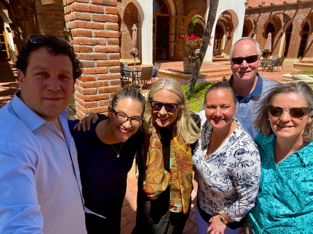 Chef Marcus Guiliano and Jamie share a delightful moment with their friends during a sunny Mexico wine tour gathering in a picturesque courtyard.