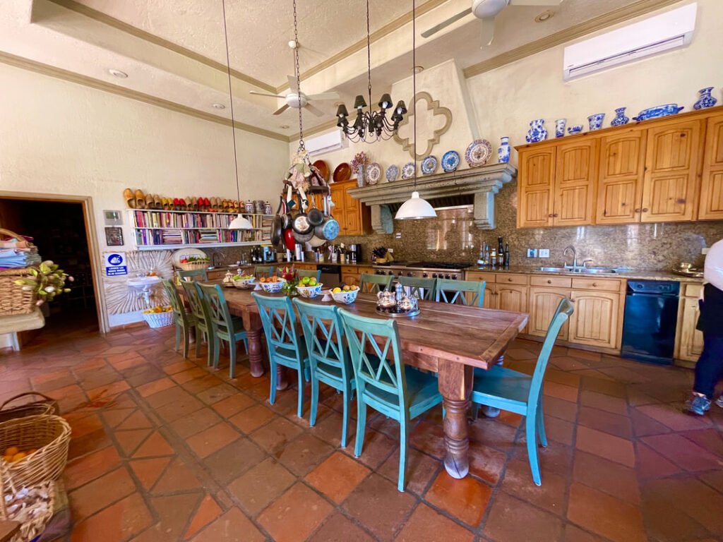 Rustic kitchen with a large wooden dining table, turquoise chairs, granite countertops, and hanging light fixtures. Mexico wine tours.