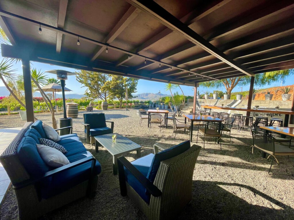 The covered patio seating area with cushioned chairs and a view of mountains in the distance is the perfect spot to unwind during Mexico wine tours.